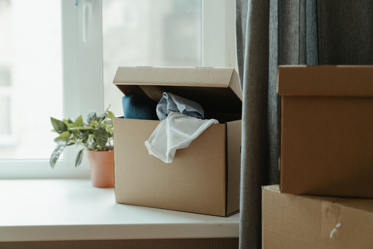 services-08 An open cardboard box filled with clothes beside a window, representing a move or relocation.